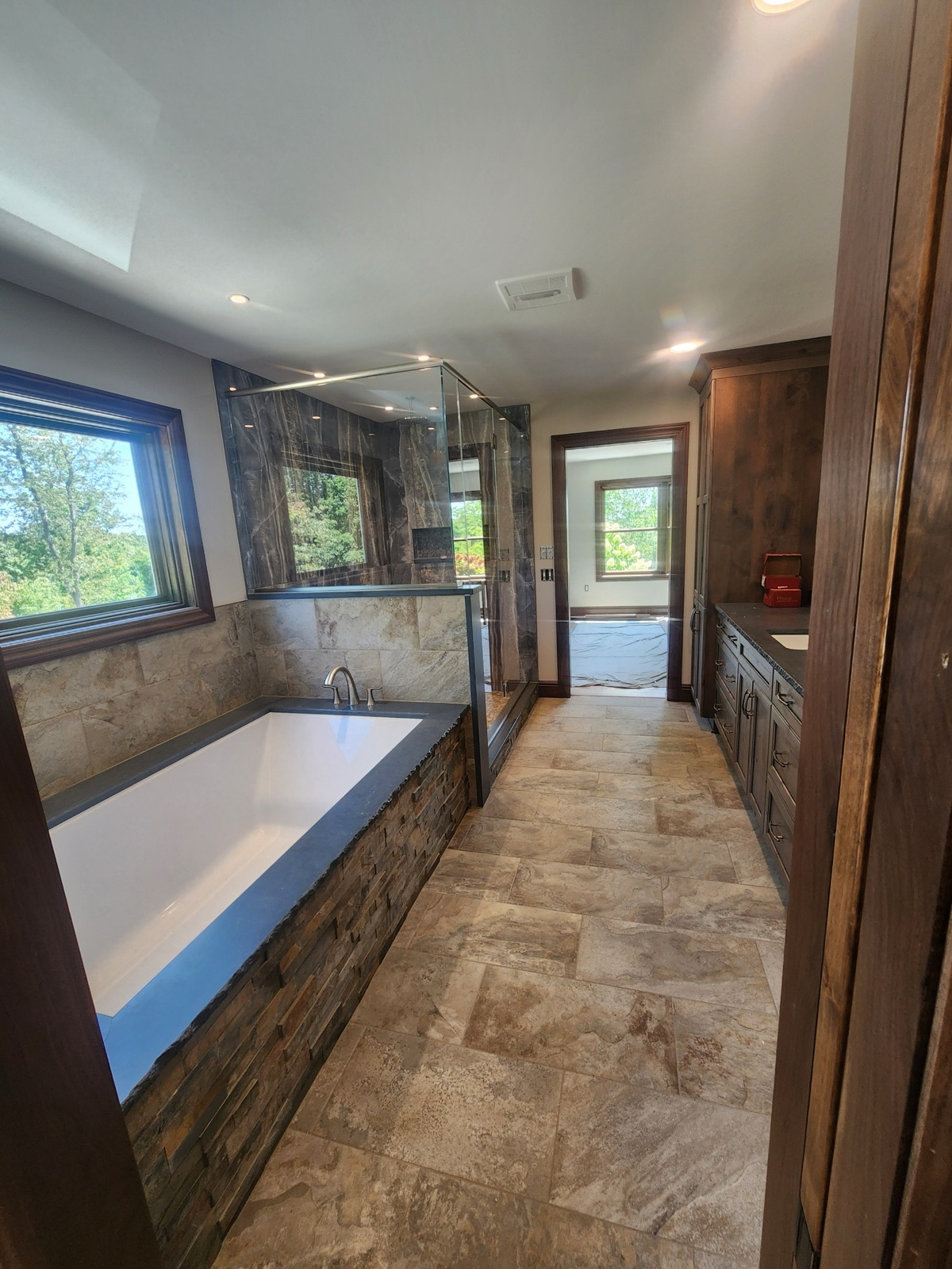 Rustic master bath with stone tub surround, dark marble shower, and forest views